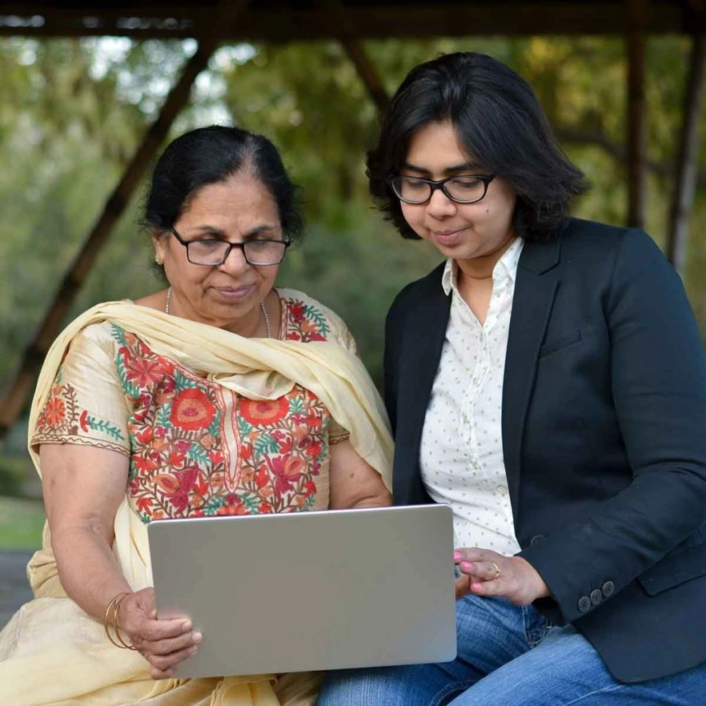 two Indian women, one elderly dressed traditionally, one younger dressed modern, both looking at laptop