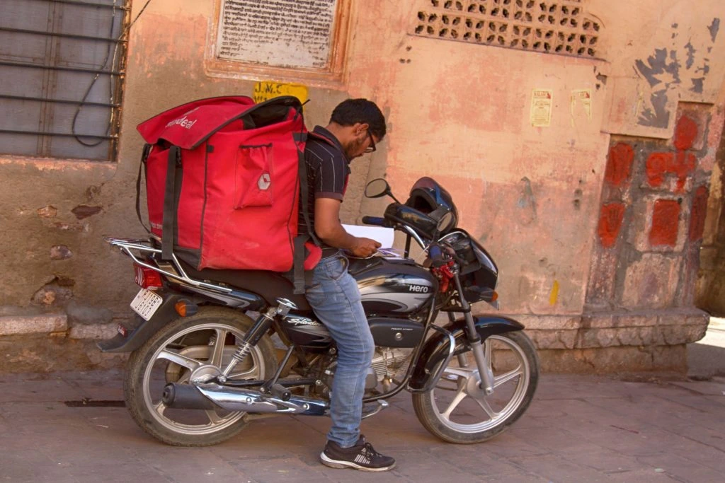 Indian man on delivery bike with red backpack for goods