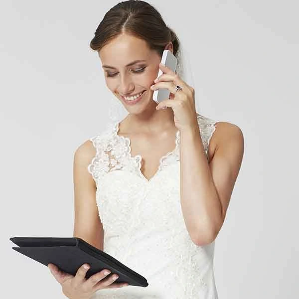 caucasian woman in wedding dress on the phone looking at tablet